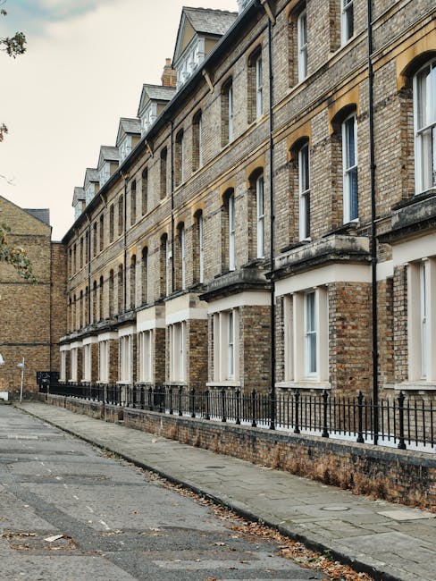 A row of Victorian terraced houses constructed with traditional yellow and brown brickwork, featuring uniform sash windows with white frames and small decorative ledges beneath each window. The buildi